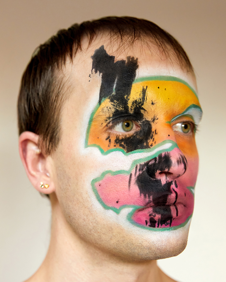 Jesse Clark posing blue and white cloud facepaint on against a sky blue background.